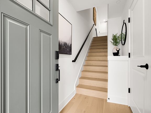 A minimalist entryway with a wooden staircase, a framed landscape artwork, and various decorative el