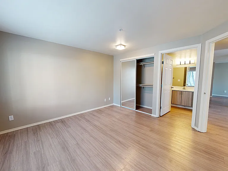 Spacious apartment bedroom with attached bathroom and wood-style flooring.