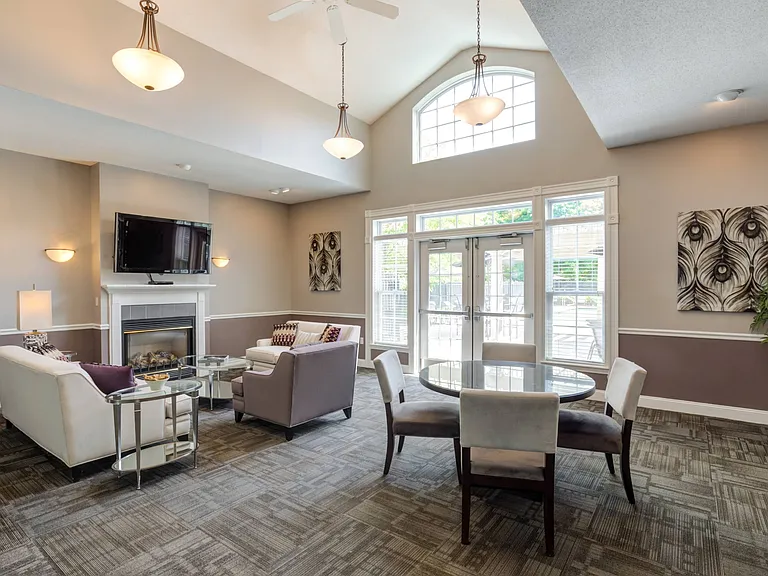 Spacious club room with comfortable seating in front of fireplace with TV and table and chairs.