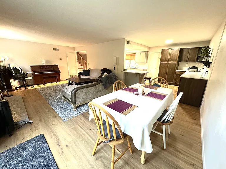 Shared open dining room into living room with piano. Wood flooring.