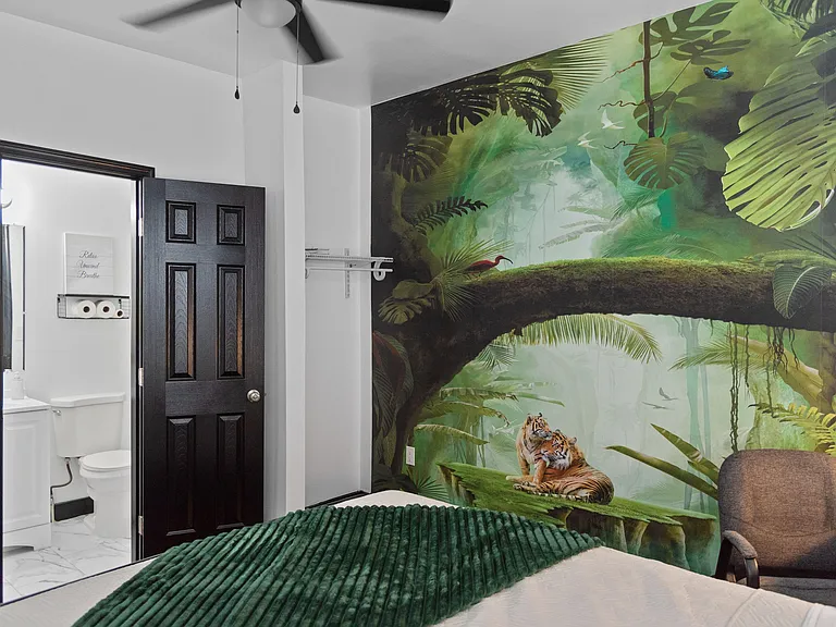 Bedroom with striking mural accent wall, ceiling fan, and convenient access to an adjacent full bath.