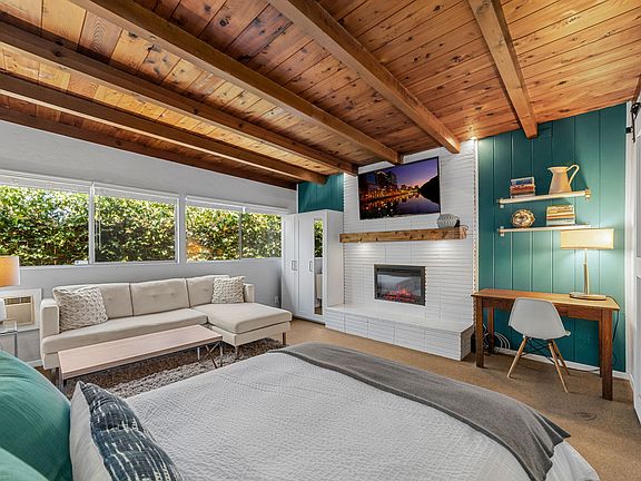 Studio guesthouse featuring open beam ceilings, fireplace and A/C, sofa, queen bed, wardrobe, 65" SmartTV and home office. Beautiful light from a wall of windows.