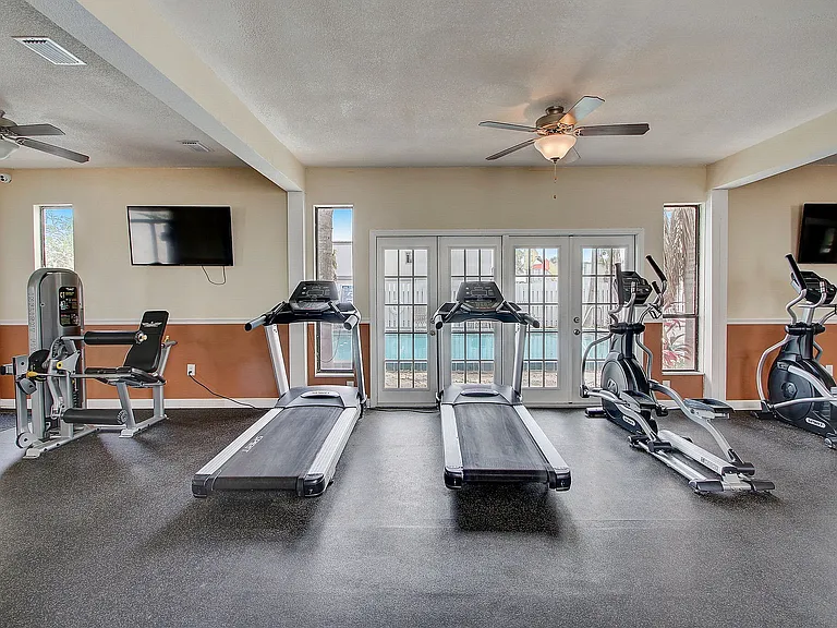 Bright and modern gym featuring top-notch equipment, including treadmills and elliptical machines, overlooking a serene outdoor pool.