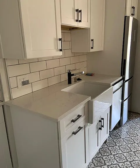 Fired clay farmers sink with andradite and stainless pull out faucet and soap dispenser. Matching andradite cabinet pulls. Garbage disposal plus pull-out, two container trash cupboard next to the sink. Under cabinet lighting.