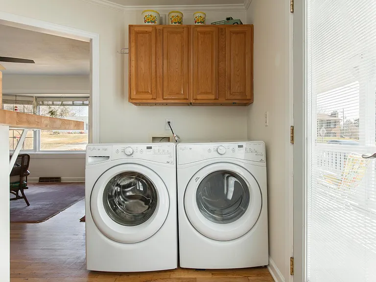 Front loading Whirlpool washer and dryer with extra cabinet storage above. This is behind the bar area in the kitchen. Double door with interior blinds off this side of kitchen leads to the wraparound porch on the side of the house.