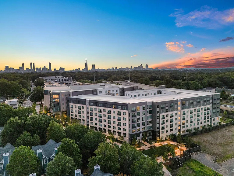 Chic urban apartment complex with modern design, surrounded by lush greenery and offering stunning sunset views of the city skyline.