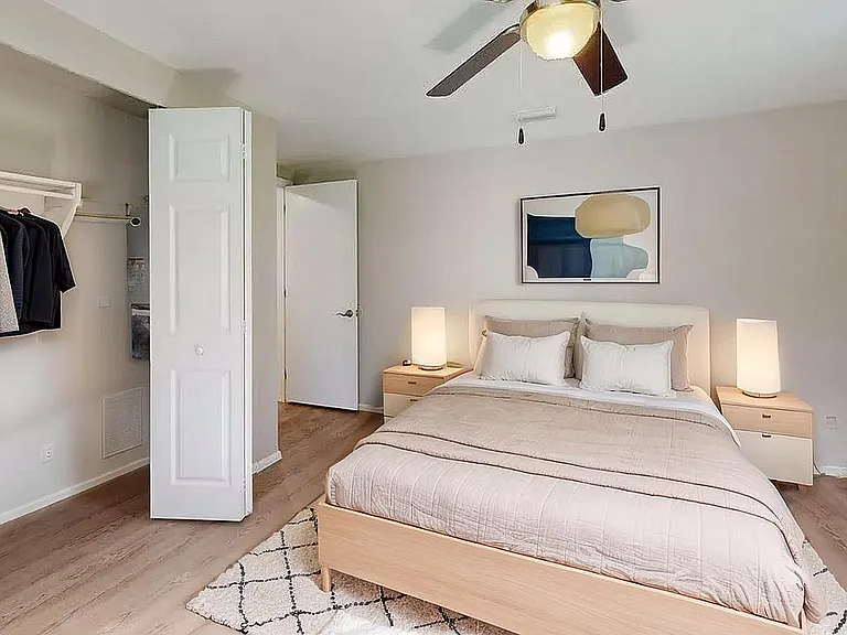 Inviting bedroom with cozy beige bedding, modern wooden furniture, and ambient lighting, complemented by a stylish open closet and chic artwork.