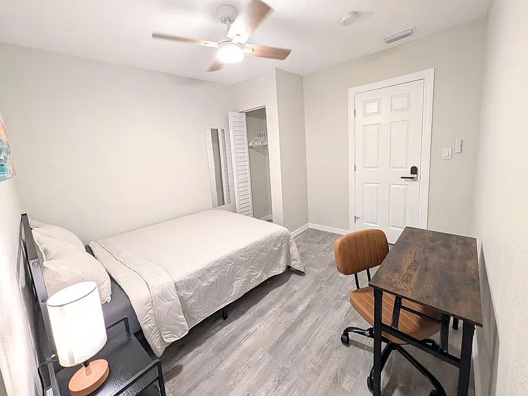 Furnished bedroom with a full bed, ceiling fan, and in-room desk, plus an open closet for easy storage.