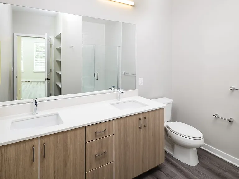 New West Phase - Finish Package IV Bathroom with double sink, white quartz countertops, oak cabinetry, and hard surface flooring