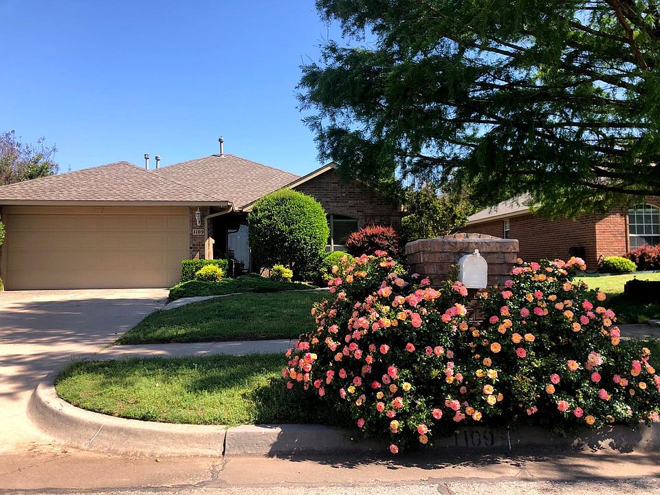 Front of home with large tree and blooming rose bushes near the mailbox