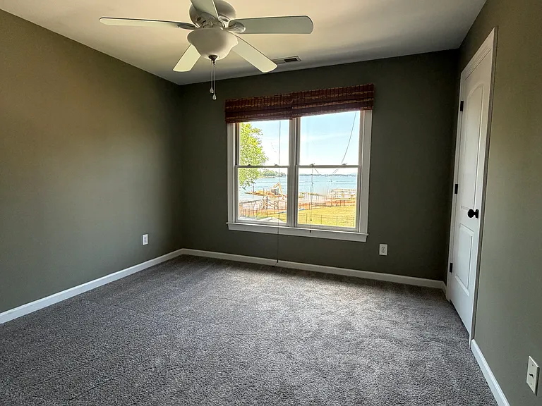Inviting secondary bedroom with a rich accent wall, soft plush carpet, ceiling fan and a large window framing direct lake views_plenty of room for a full bed, plus a closet to keep the space organize.