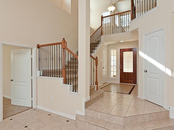 Beautiful tiled foyer with high ceilings, ceramic tiled floors and patterned inset.  A dramatic wood stained and wrought iron staircase leads to the second level with balcony views from above. A half bath is located near the front door.