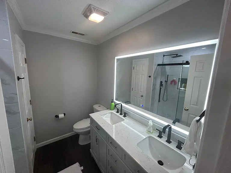 Remodeled primary en-suite bathroom featuring modern lighted mirror, walk-in shower, and double vanity.