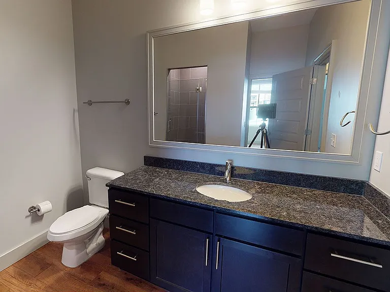 Apartment bathroom with glass enclosed shower and wood-style flooring.