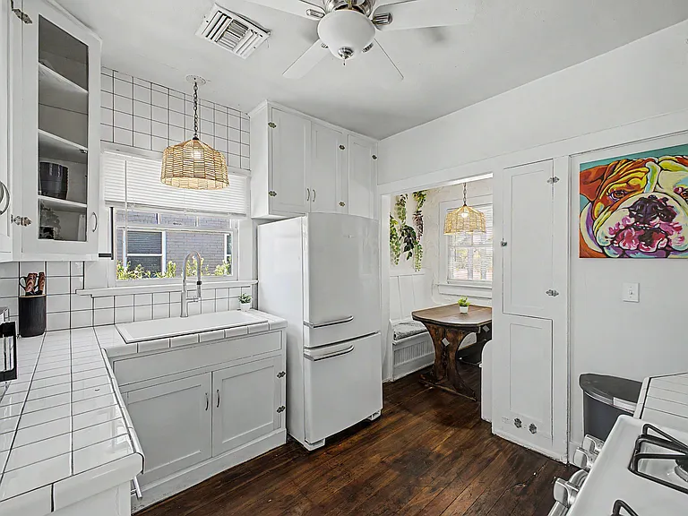 Efficient kitchen with ample white cabinetry, tiled counters and backsplash, full-size fridge, and space for a small dining n