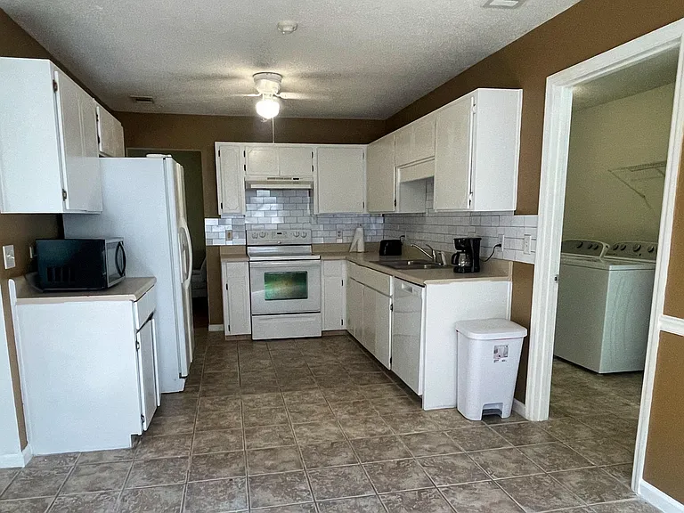 Spacious kitchen with ample white cabinetry, generous counters, tile backsplash, and full appliance package plus laundry nook