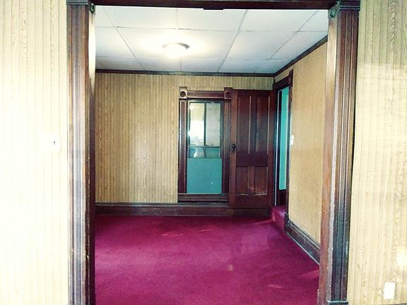 This is a view through the original wood archway of the third living space, which is on the northwest corner of the house. Access to the two bedrooms upstairs is through the door on the right. The front door on the west side of the house leads into the