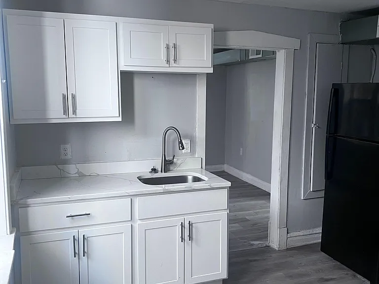 Kitchen area with Shaker-style cabinetry, stainless sink, and a refrigerator nook off the main living space.