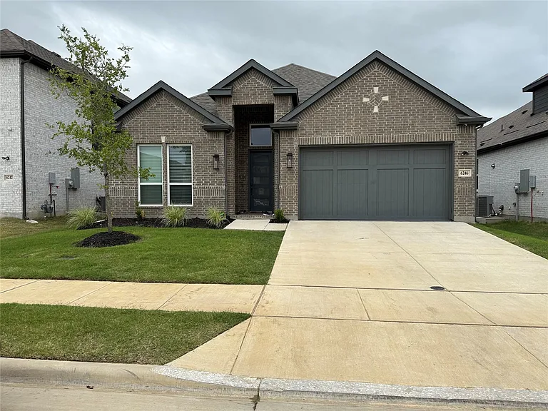 Contemporary brick exterior featuring a dark gray garage door, concrete driveway, and manicured lawn with landscaping
