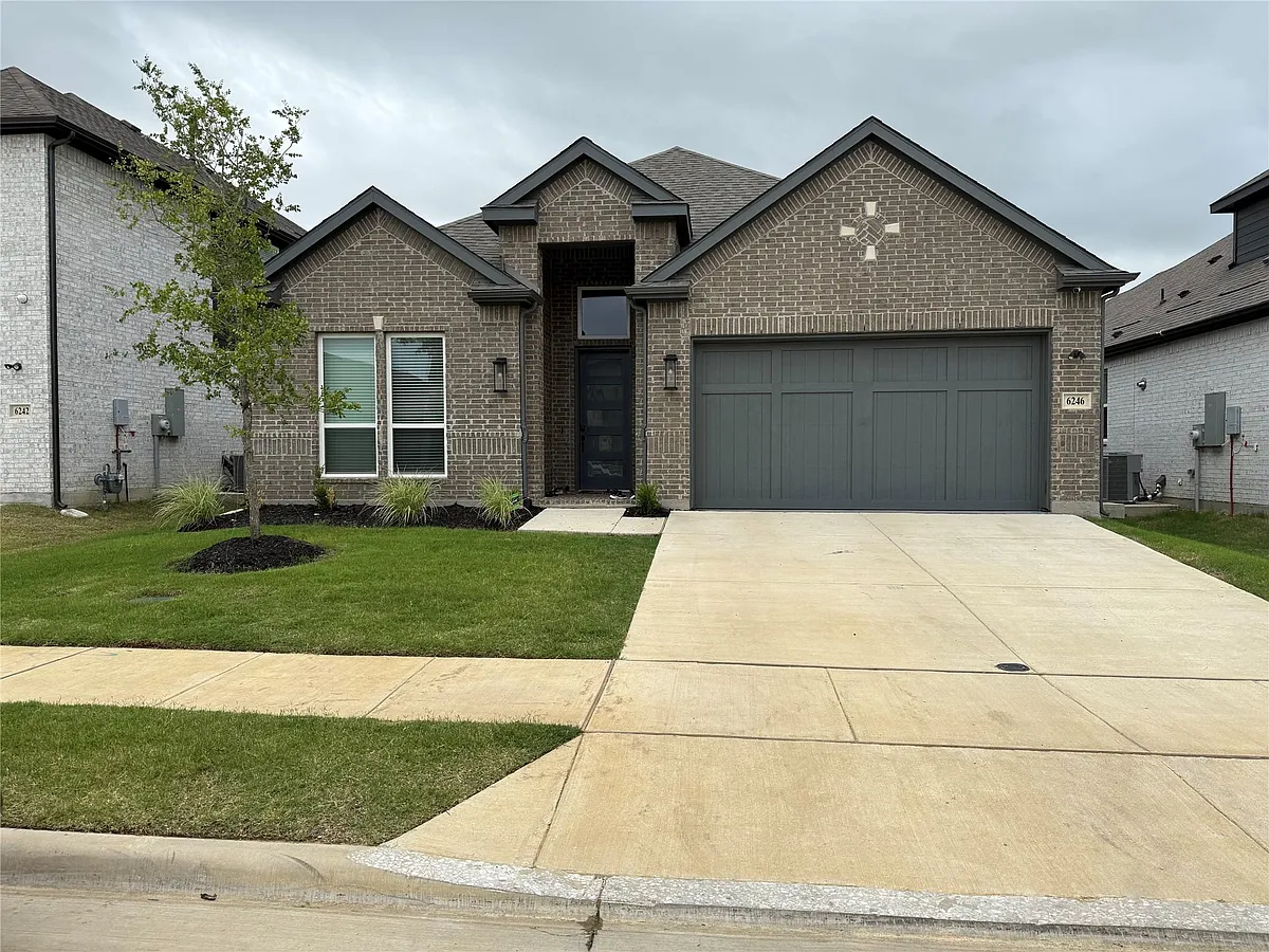 Contemporary brick exterior featuring a dark gray garage door, concrete driveway, and manicured lawn with landscaping - 6246 Shasta Creek Rd