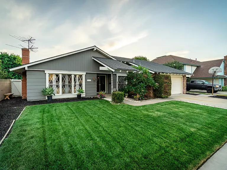 The front of the Ranch Style house with 2 car garage and driveway, On your left side is a small white door leading to the side backyard.