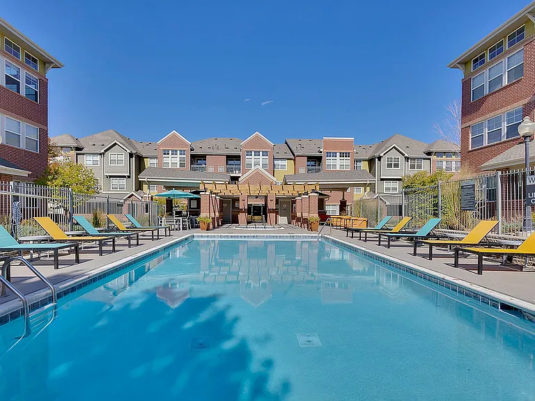 Inviting outdoor pool area at modern apartment complex, featuring colorful lounge chairs and landscaped surroundings under a bright blue sky.