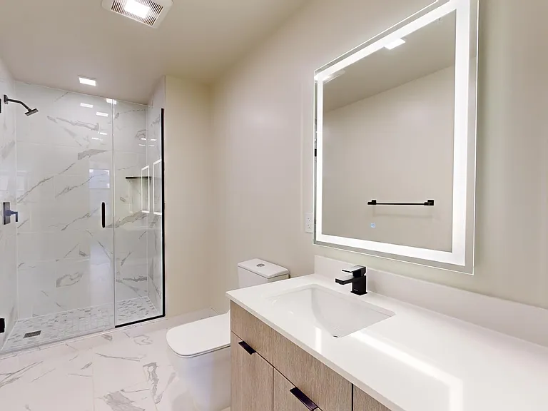 Apartment bathroom with glass-enclosed shower, tile flooring, and LED vanity mirror.