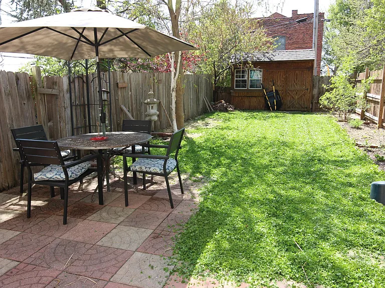 The backyard featuring a patio, grass, and a large lockable garden storage shed.