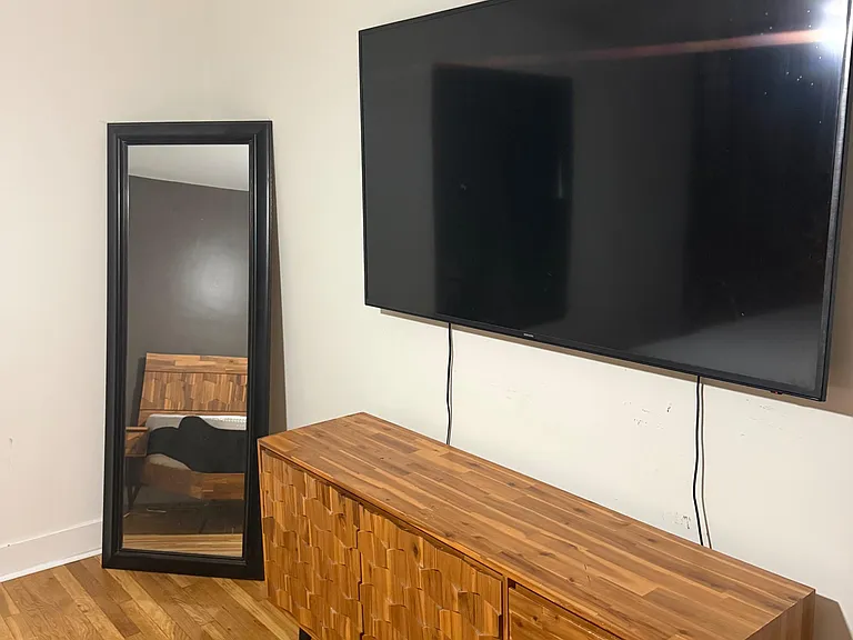 Shared living area with hardwood floors, a wall-mounted TV, and a storage console for media and personal items.