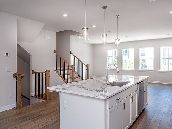 A modern, open-concept kitchen with a marble-topped island, wooden floors, and a staircase leading t