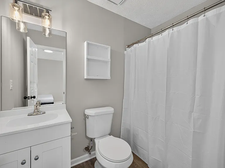 Full bathroom with a single-sink vanity, mirrored cabinet, open shelving, and a shower/tub with curtain.