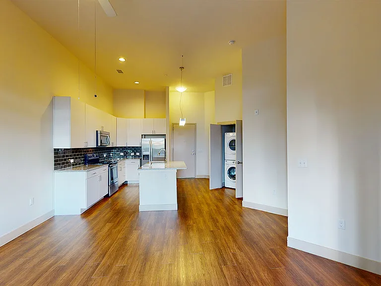 Apartment kitchen with stainless steel appliances, dining and living room with wood-style flooring.