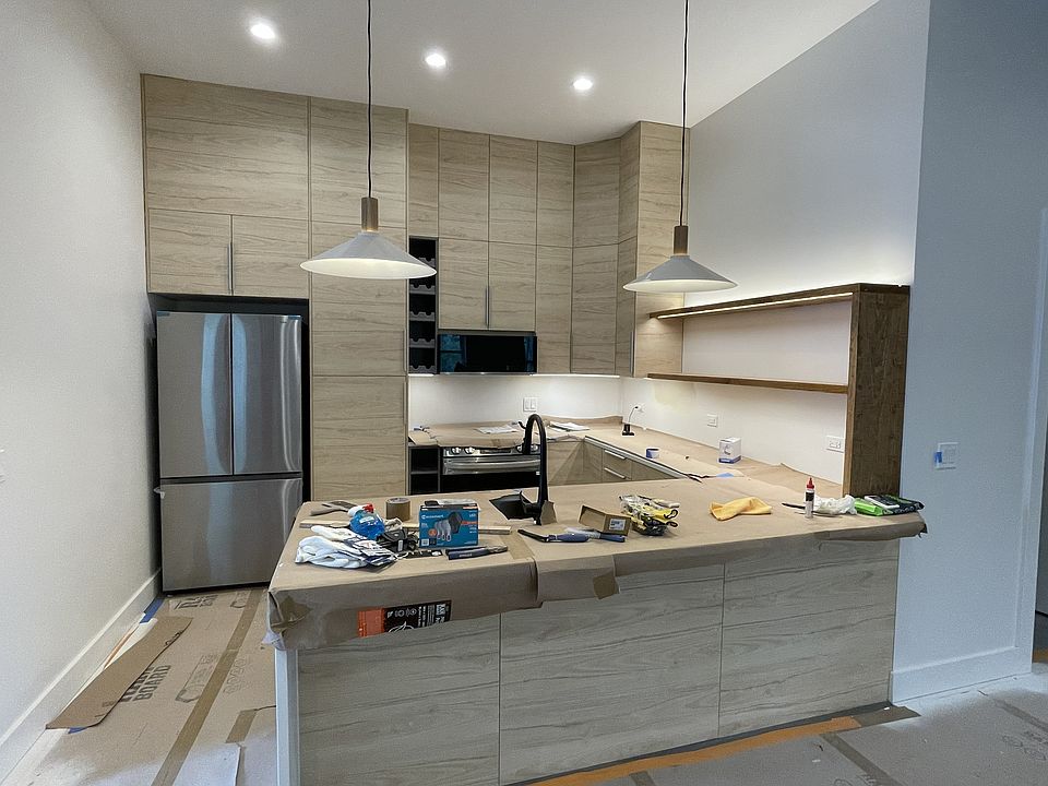 In progress phot of kitchen. Has an island with room for stools. Under cabinet lighting, new appliances.