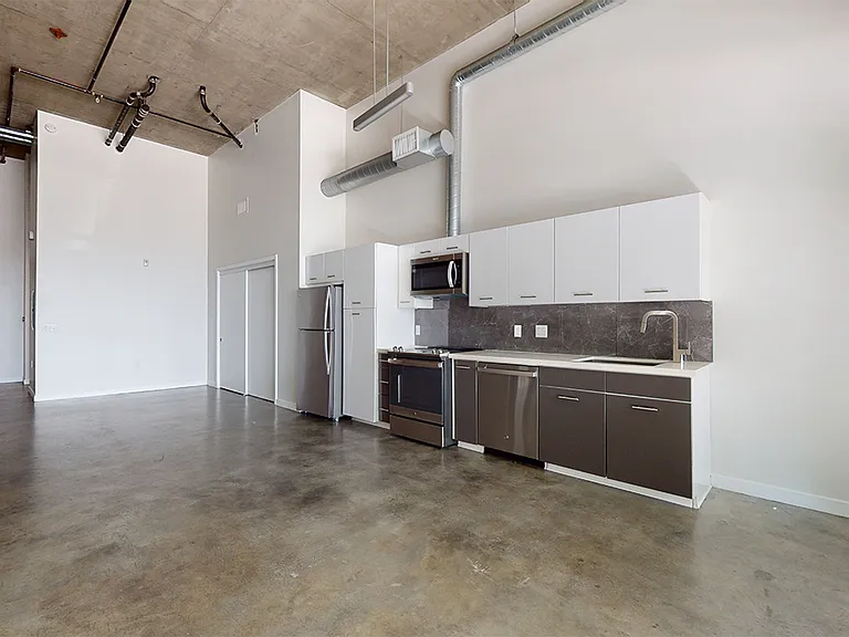 Apartment kitchen with stainless steel appliances, dining and living room with polished concrete or wood-style flooring.