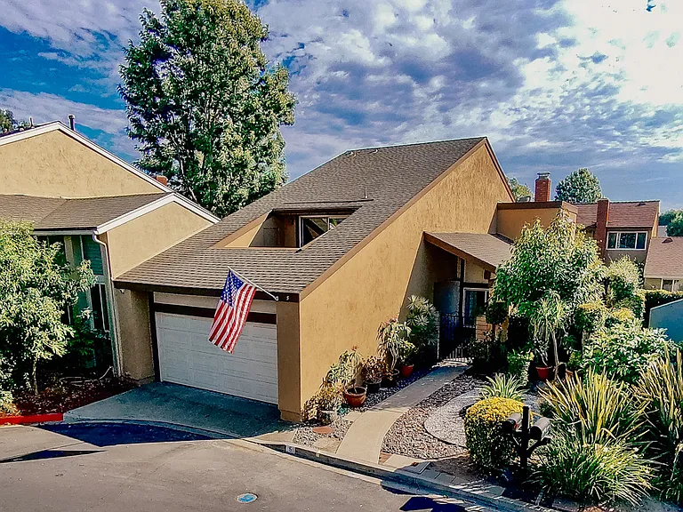 Front of charming home with attached two-car garage, master bedroom balcony visible, with the warm, inviting front yard.