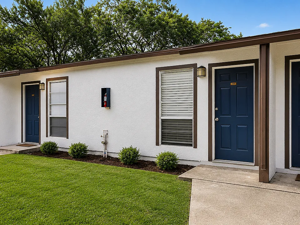 Charming apartment entrance with fresh white facade, blue doors, and lush green lawn.