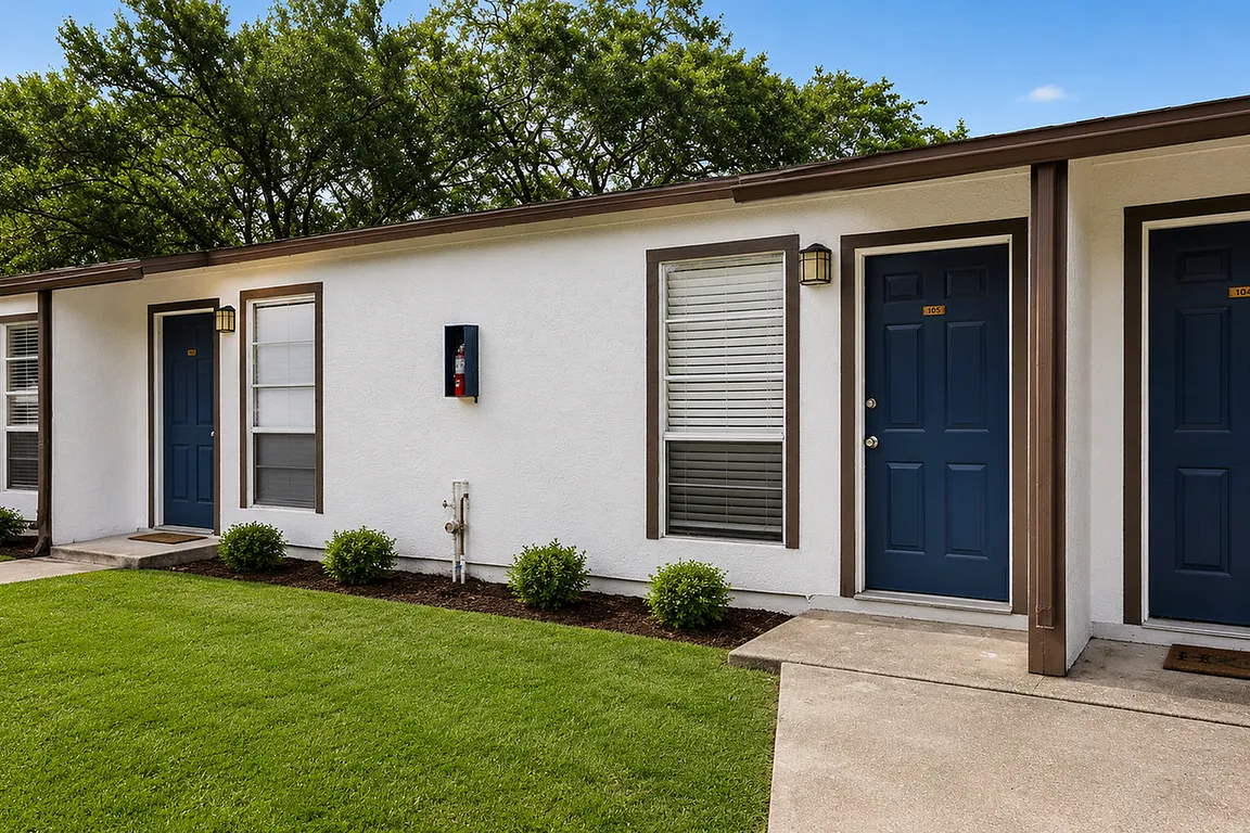 Charming apartment entrance with fresh white facade, blue doors, and lush green lawn.