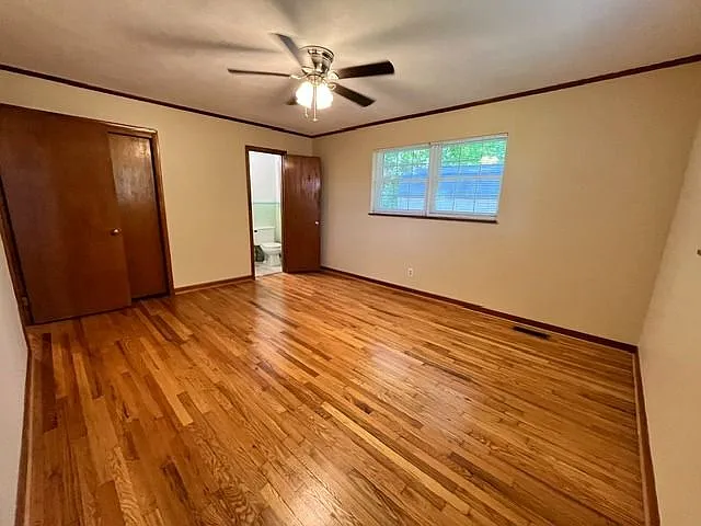 Spacious primary bedroom featuring gorgeous hardwood floors, neutral paint tones, and plenty of natural light. This inviting room offers a functional layout with direct access to a private bathroom and ample closet space. Complete with warm wood trim, a m