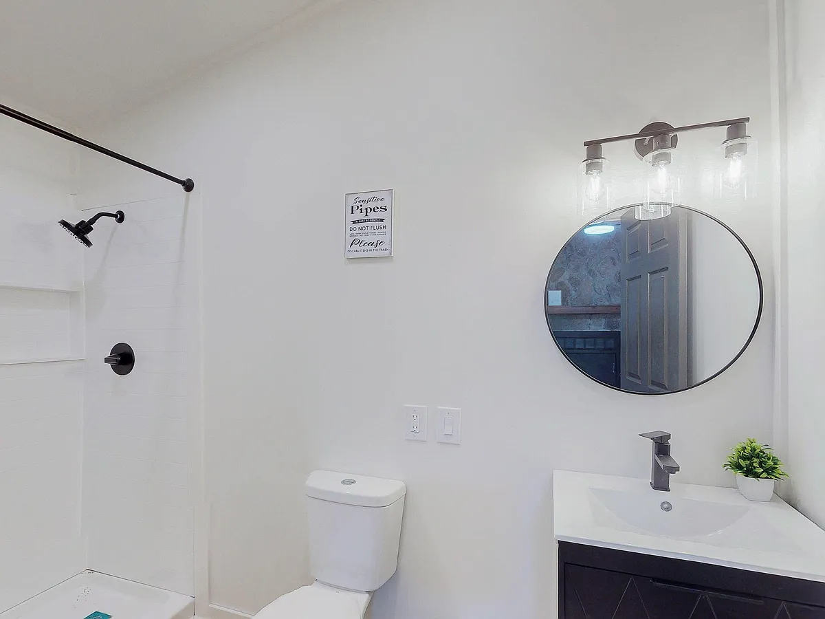 Clean bathroom with walk-in shower, contemporary vanity and round mirror, plus updated lighting and fixtures. - Satellite Blvd