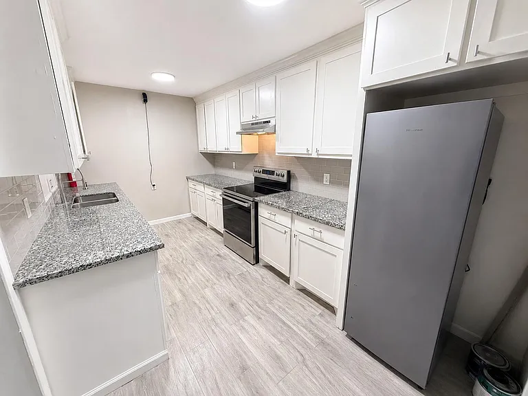 Galley kitchen with shaker cabinetry, granite-look counters, tile backsplash, and stainless range plus full-size fridge.