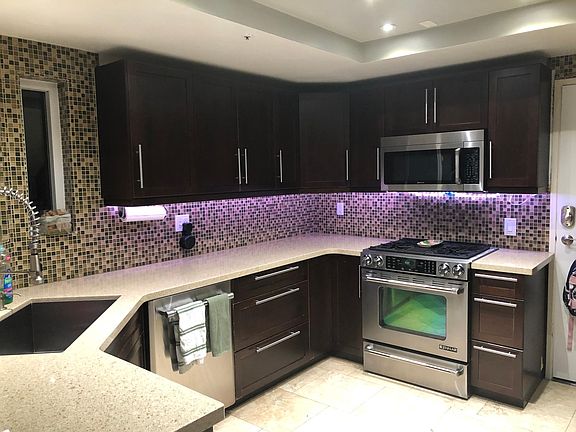 Kitchen with travertine floors, under cabinet LED lighting, and a JennAire has range.
