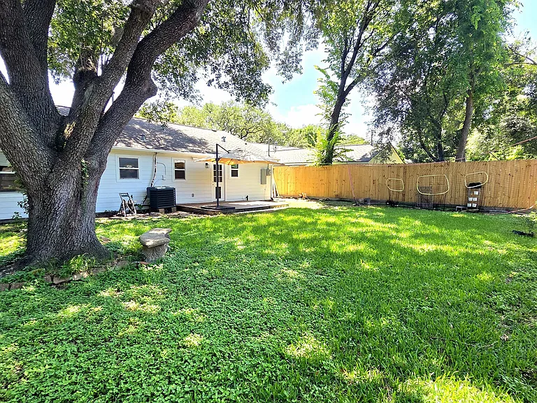 Spacious backyard with lush grass, mature trees providing shade, a wooden fence for privacy, and a deck area. Ideal for outdoor activities and relaxation.