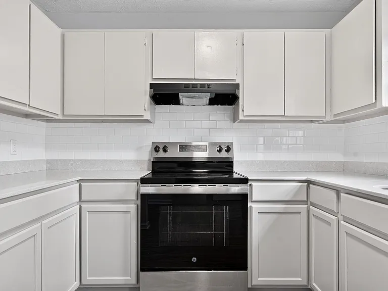 U-shaped kitchen with ample cabinet storage, generous counters, and an electric range with vent hood and tile backsplash.