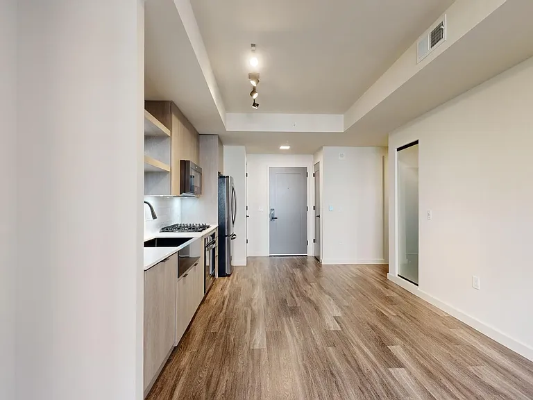 Apartment kitchen with black stainless steel appliances, dining and living room with wood-style flooring.