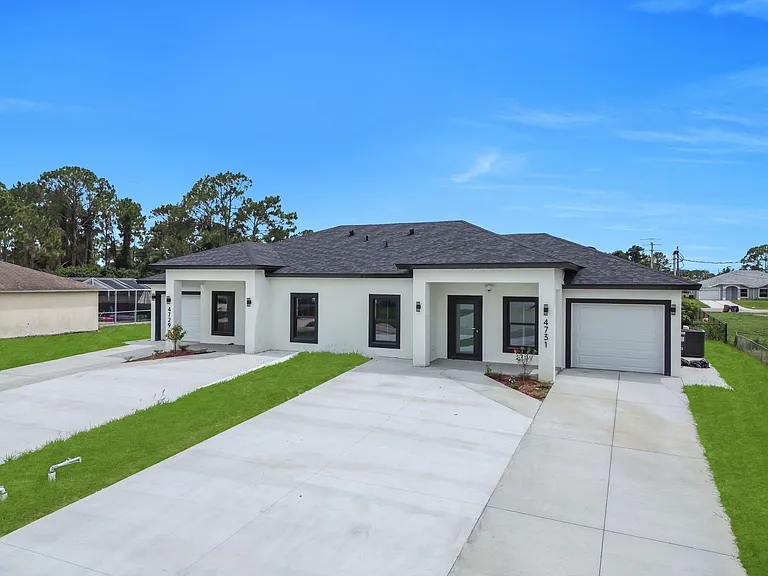 Single-story duplex-style exterior with fresh stucco finish, wide driveways, covered entries, and a tidy front lawn.
