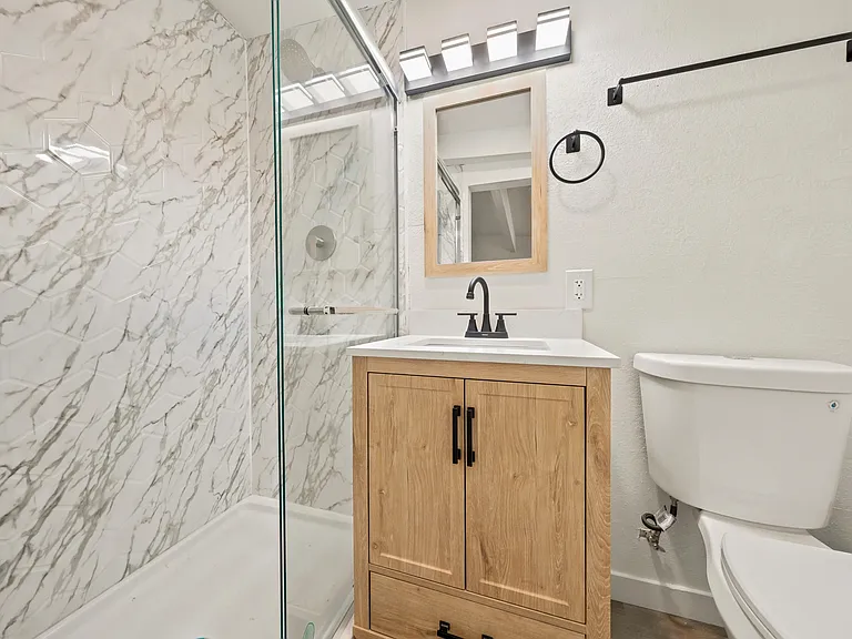 Updated bathroom with a glass-enclosed tub/shower, stone-look tile surround, and a vanity with storage and mirror.