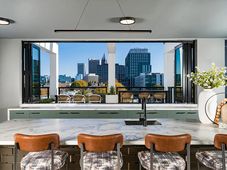 A shared kitchen and bar at Modera Westside Trail with expansive windows, skyline views, and seating designed for larger gatherings at home.
