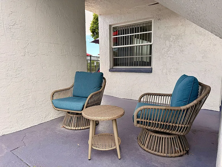 Charming patio corner featuring two stylish wicker chairs with teal cushions and a matching round table, perfect for relaxing.