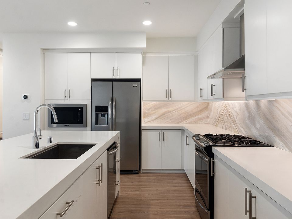 Spacious, modern kitchen featuring stainless steel appliances, quartz countertops, marble accents, and ample cabinet space