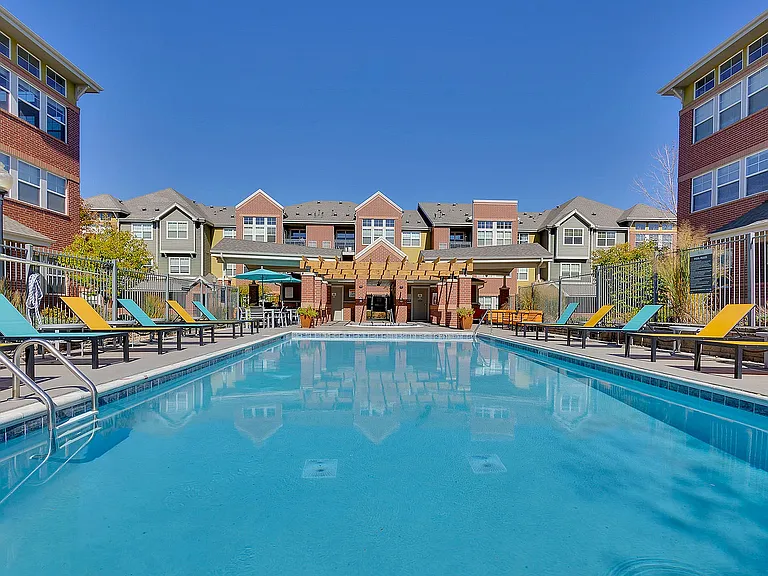Inviting apartment complex with colorful lounge chairs by a sparkling pool, perfect for relaxation and enjoyment.